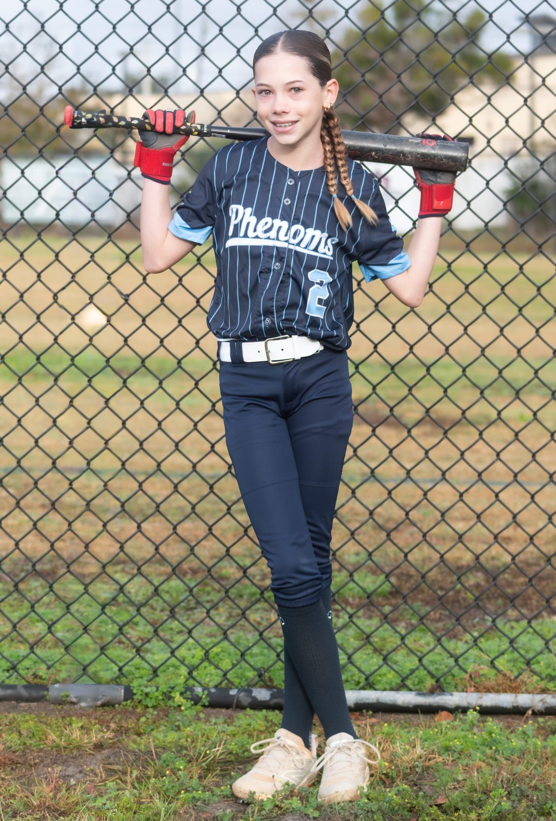 Camden with a bat across her shoulders in a navy pinstripe Phenoms uniform